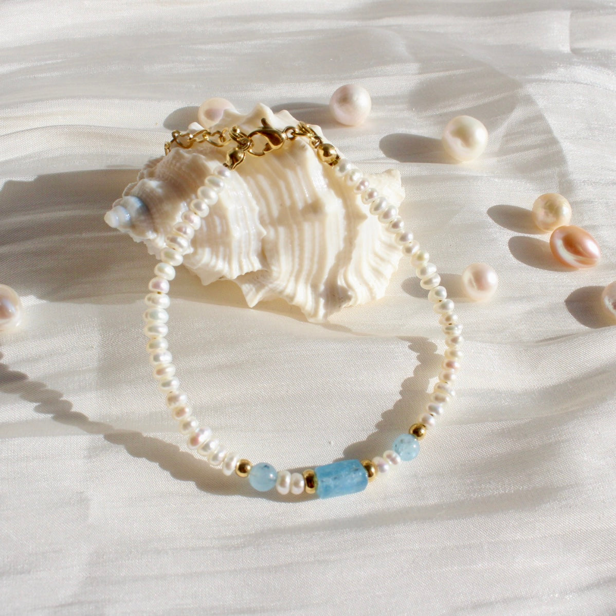 Pearl and aquamarine beaded bracelet with gold accents on a seashell, elegant jewelry