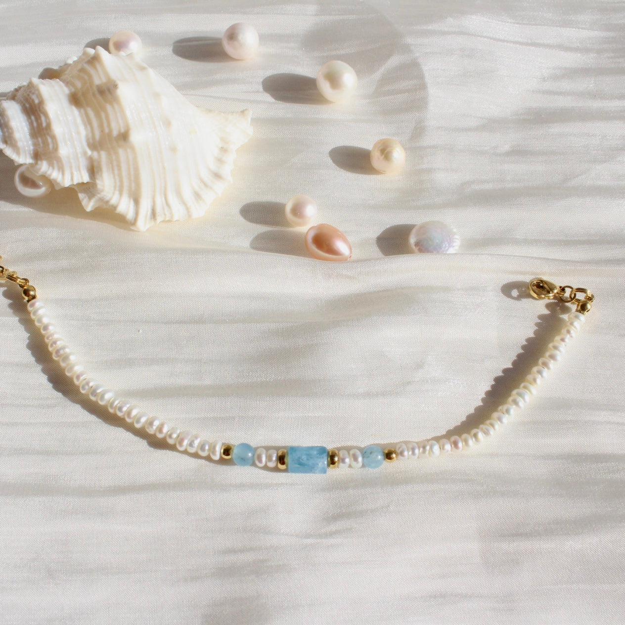 Perlenarmband mit blauen Edelsteinen und goldenen Details auf Seide, Muschel und Perlen